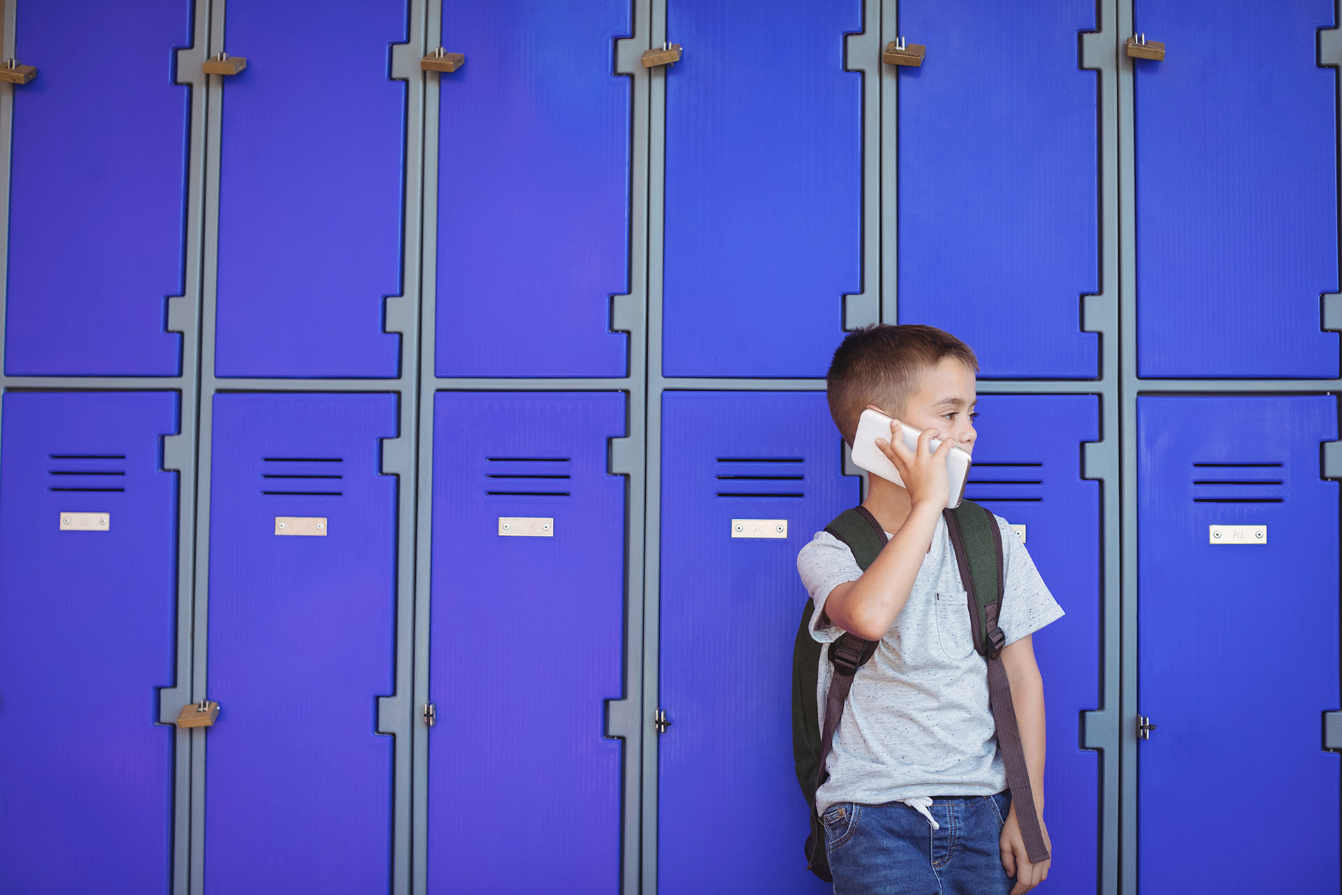 Elementary boy talking on mobile phone against lockers